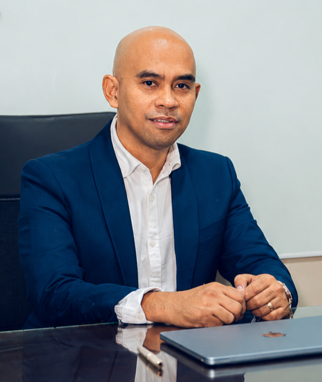 Mark Jim Acosa in a blue suit at his office desk
